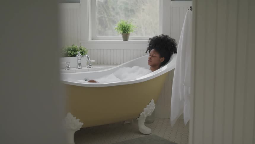 Female closes her eyes as she soaks in a claw foot bathtub filled with bubbles