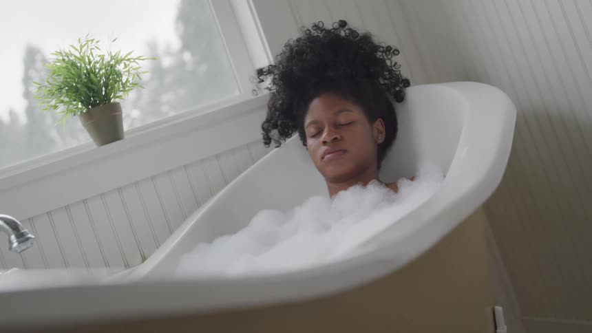 Females eyes are closed as she soaks in a claw foot bathtub filled with bubbles