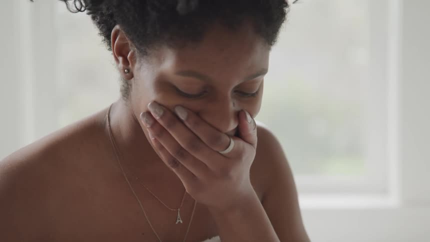 A woman wearing only a towel in a bathroom looks at the results of a pregnancy test and gets excited
