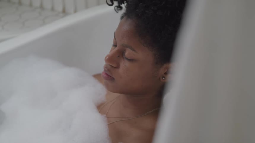 A young black woman relaxes in a bubble bath with her eyes closed