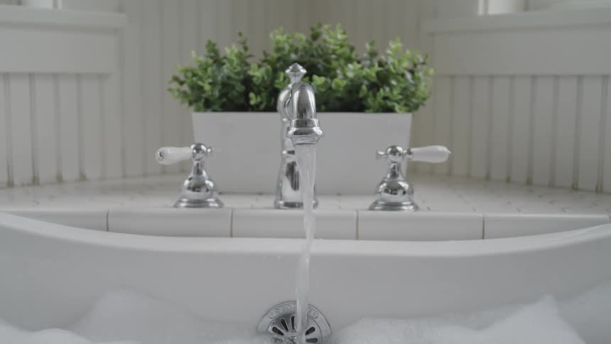 Silver faucet fills a bubbly bathtub with water in a bathroom