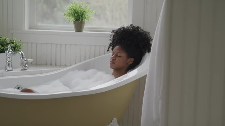 A young woman rests her eyes while taking a bubble bath