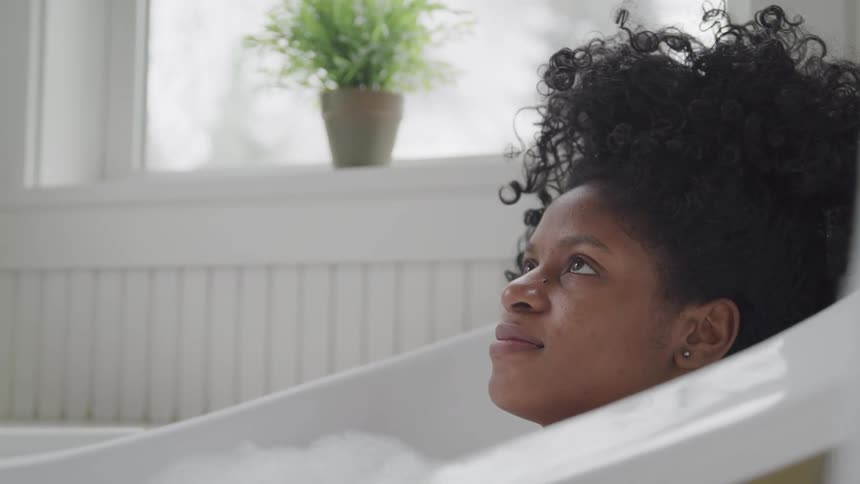 Female resting her head on the back of the tub as she soaks in a bubble bath and stares up at the ceiling