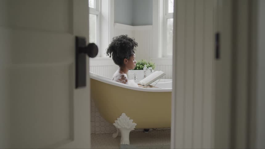 Woman in a vintage claw foot bathtub taking a bubble bath reading a book