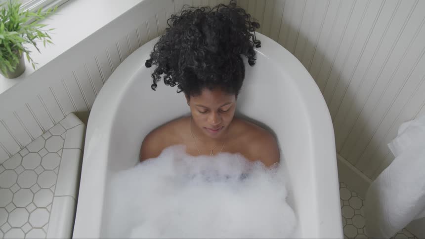 A black female soaking in a sudsy bathtub