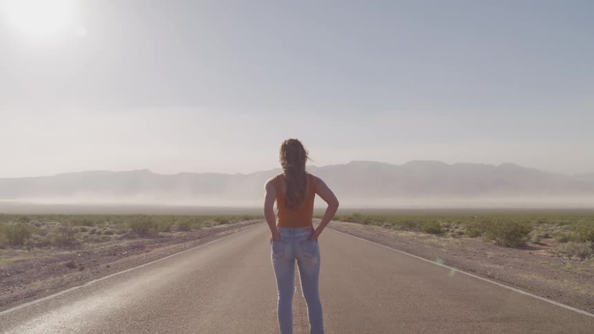 A woman is standing in the middle of the empty highway