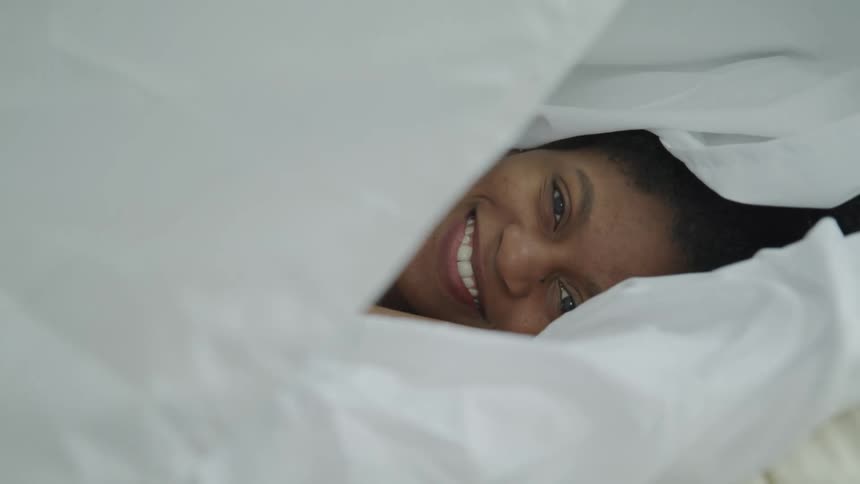 Woman laying on bed smiles as blanket falls across her