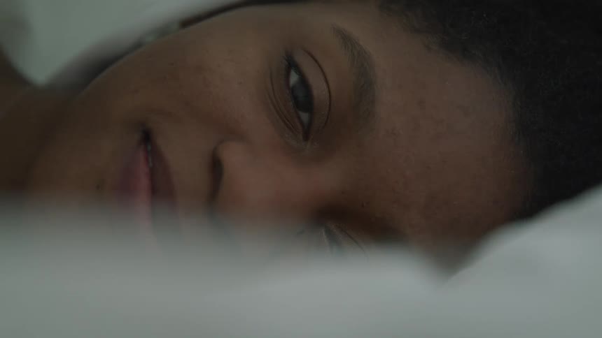 Close up of a womans face laying in bed covered in white bed sheets