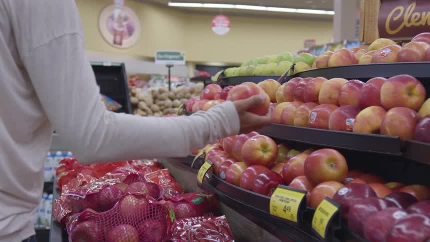 A woman picks up an apple in a grocery store