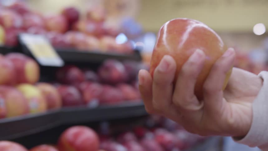 Man picks apple from produce section placing it in handheld basket