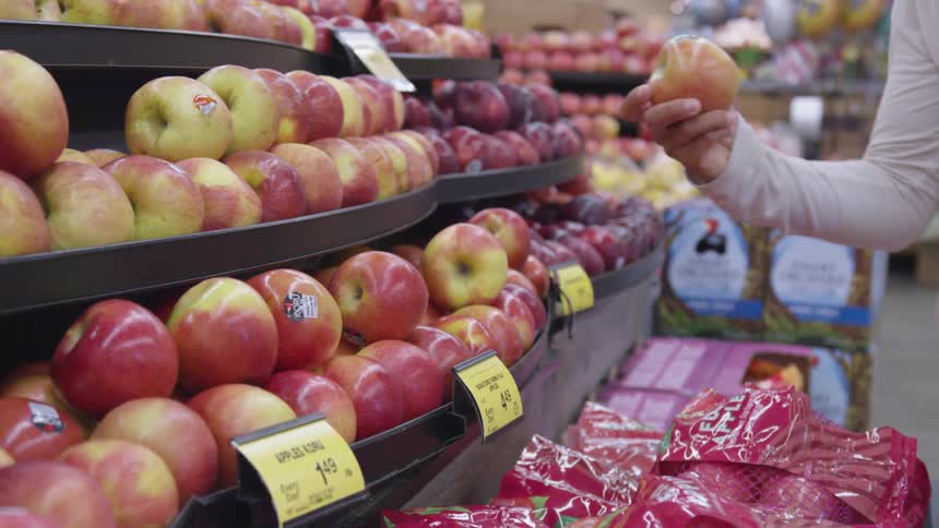 A person in a supermarket taking an apple from a shelf