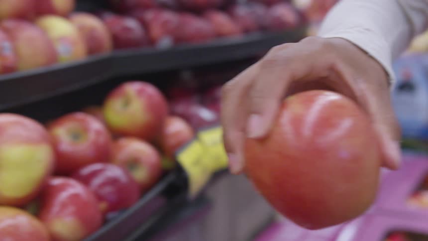 Young woman picks up apples from the supermarket shelf into a grocery basket