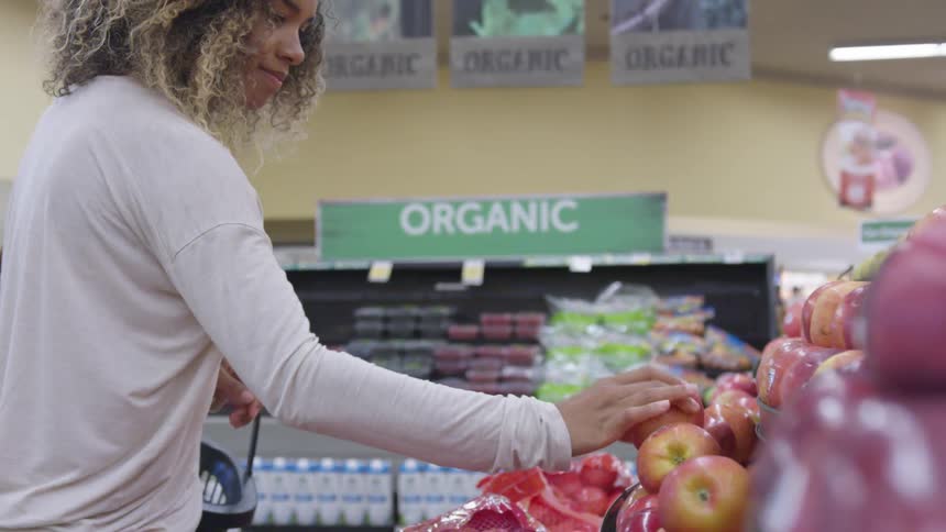 Young woman carrying a basket buys red apples in the supermarket
