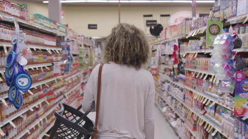 A woman walks down an aisle in a grocery store