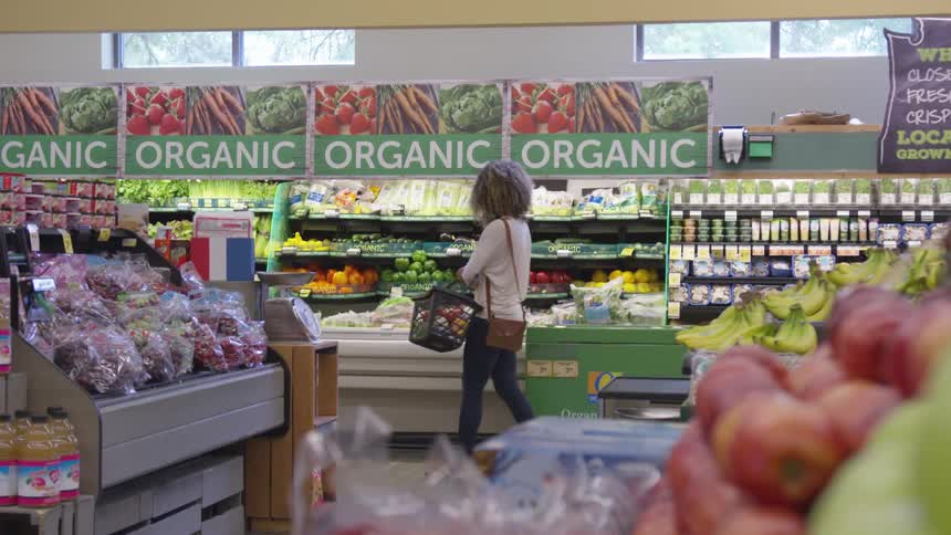 A woman walks through the produce section of a grocery store looking at the items