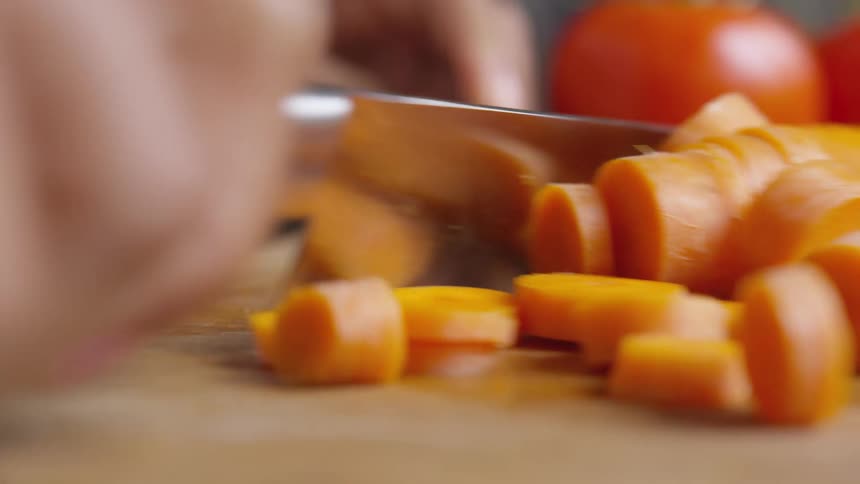 Cut carrots being swept across a cutting board with a knife