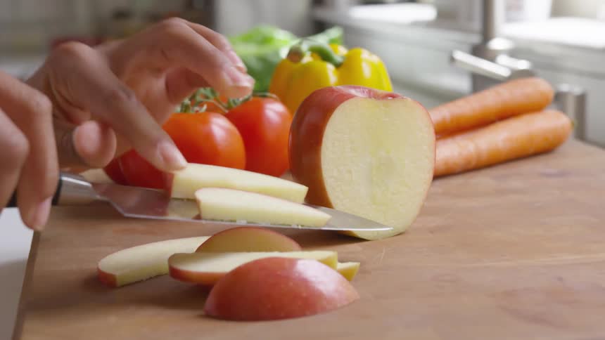 A women carefully slices and apple into thin pieces on a wooden cutting board