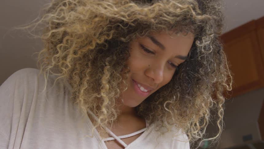 A young woman at home looks down and smiles