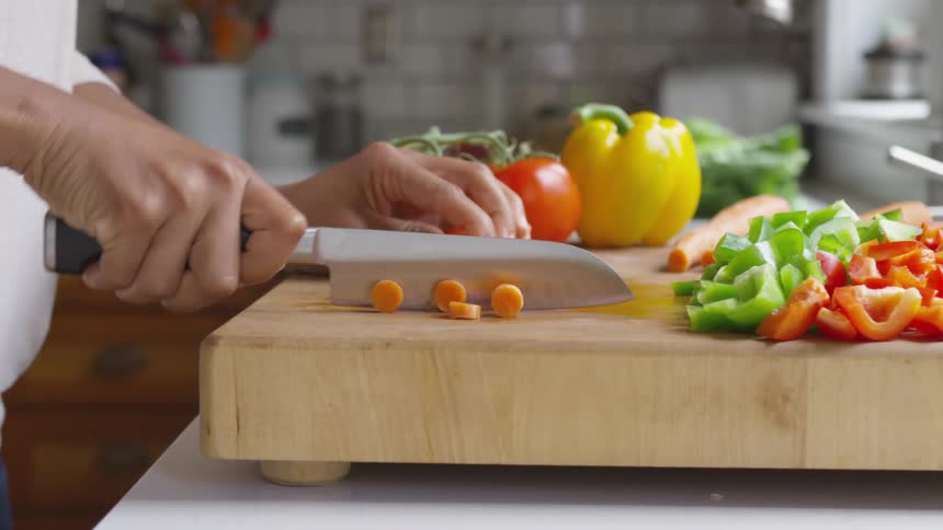 Person chops carrots and other vegetables on thick slab of chopping board sitting on counter
