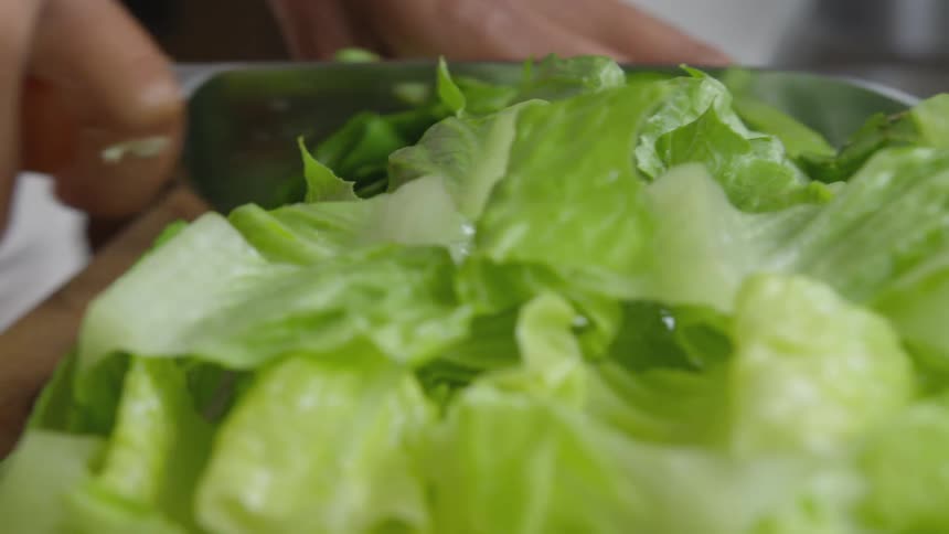 Close up of lettuce being cut by a person