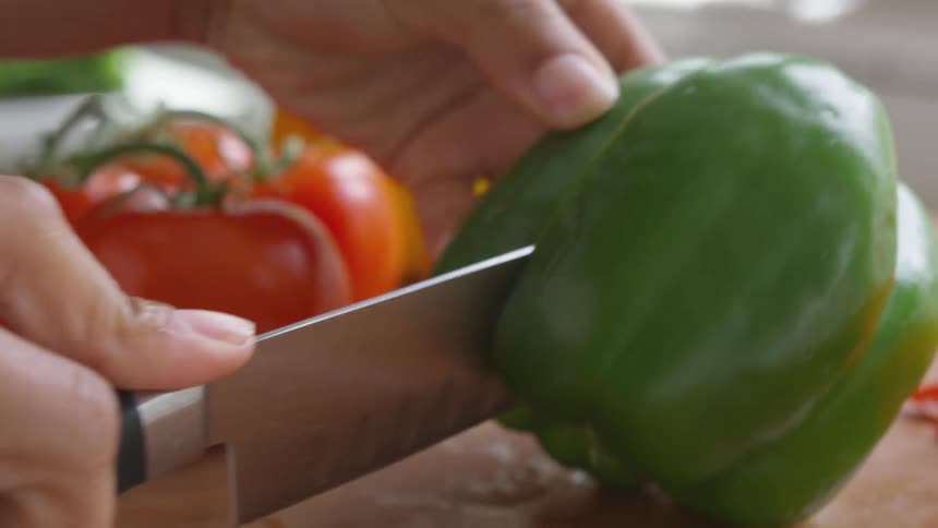 A person uses a knife to slice a bell pepper on a wooden cutting board