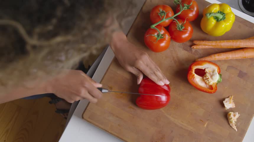 An overhead view of a woman slicing vegetables on a cutting board in a home kitchen during the day