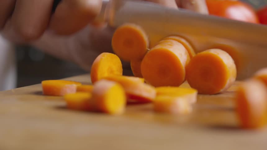 Mans hands cut a carrot on a cutting board in the kitchen
