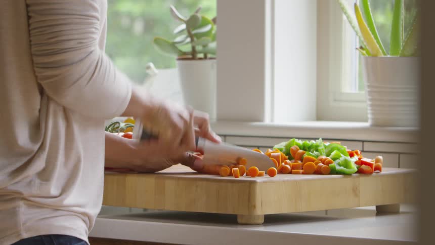 Chopping carrots with a sharp chefs knife on a wood cutting board