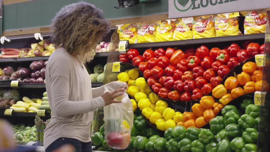 A female customer in a grocery store puts colorful bell peppers in a bag