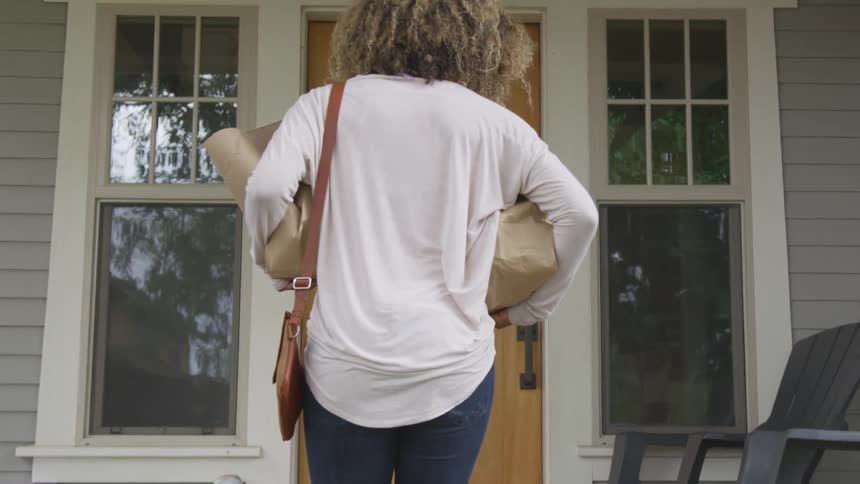 Walking up to front door carrying two brown bags