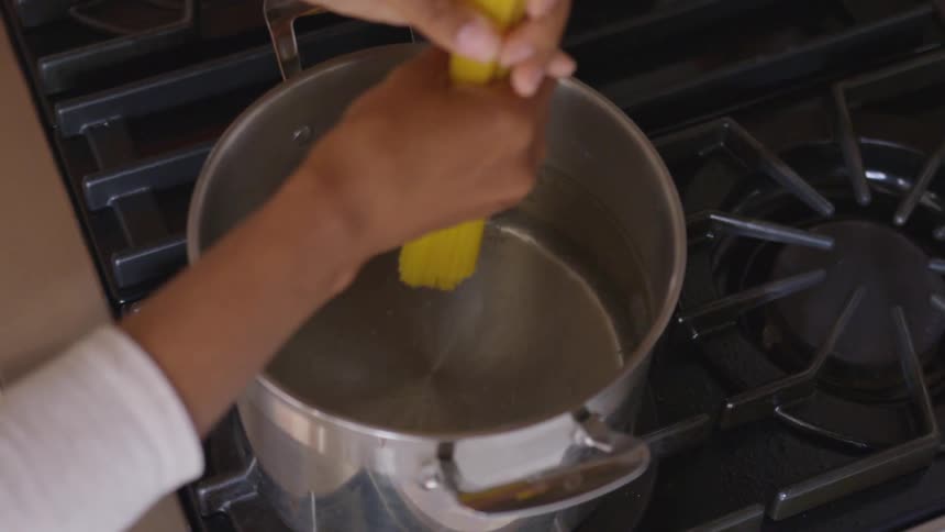 A person dropping pasta into a boiling pot of water on a gas stove