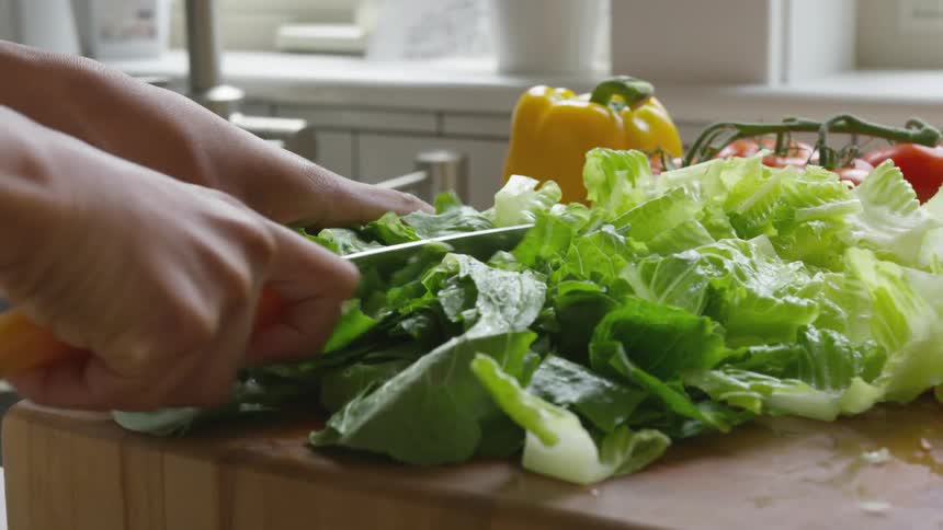 A person in a kitchen chopping vegetables with a knife on a cutting board