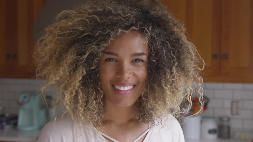 Woman stands in kitchen next to cabinets smiling widely