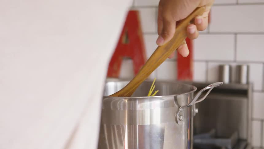 A cook uses a ladle to stir pasta in a steaming pot