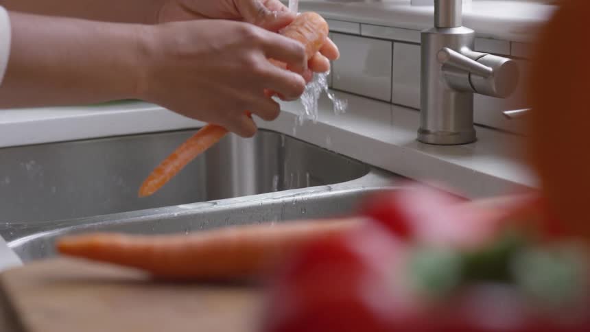 A person picks up a carrot from a cutting board and rinses it in a kitchen sink