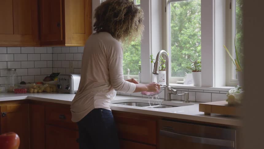 A woman stands at her kitchen sink and washes fruit
