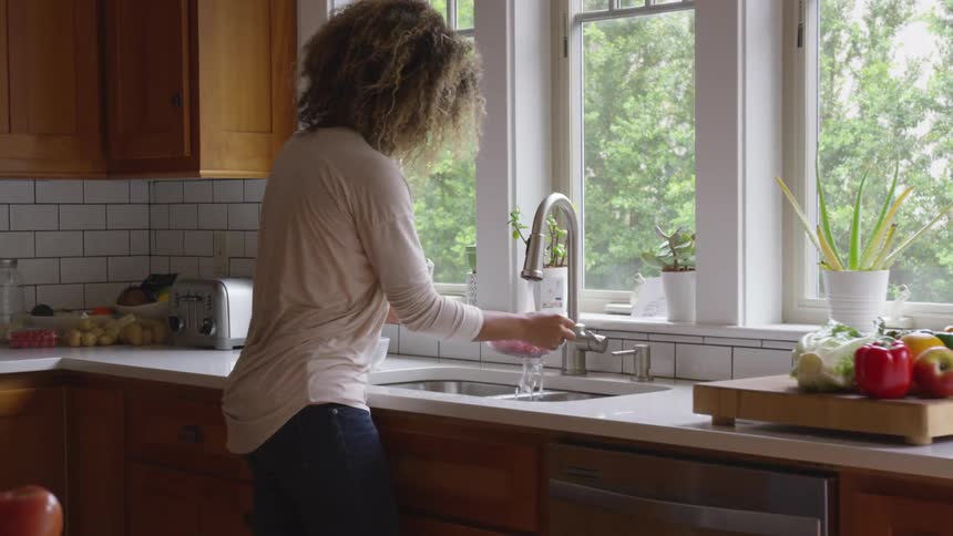 A woman washes a bowl of cherry tomatoes under a kitchen faucet