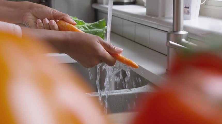 A woman stands at her kitchen sink as she rinses off a whole carrot
