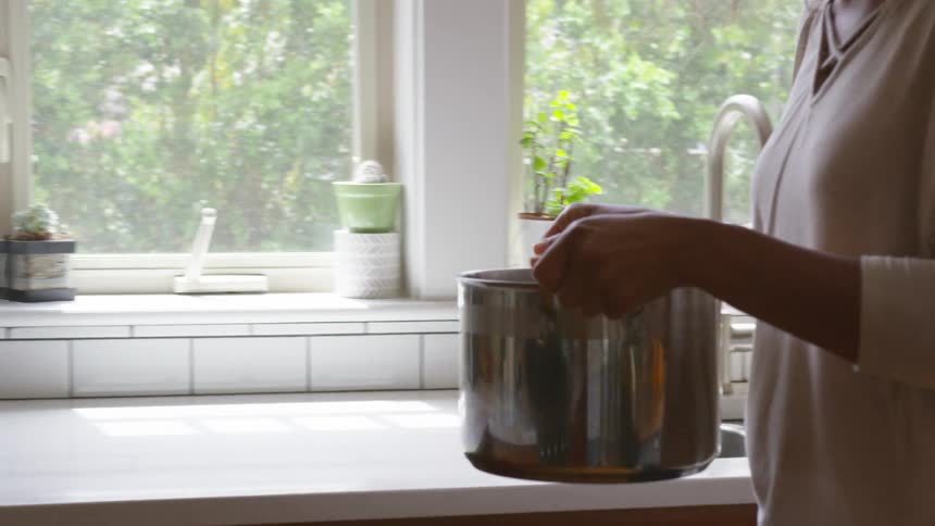 A woman fills a metal pot with water and then carefully carries it over to the stove