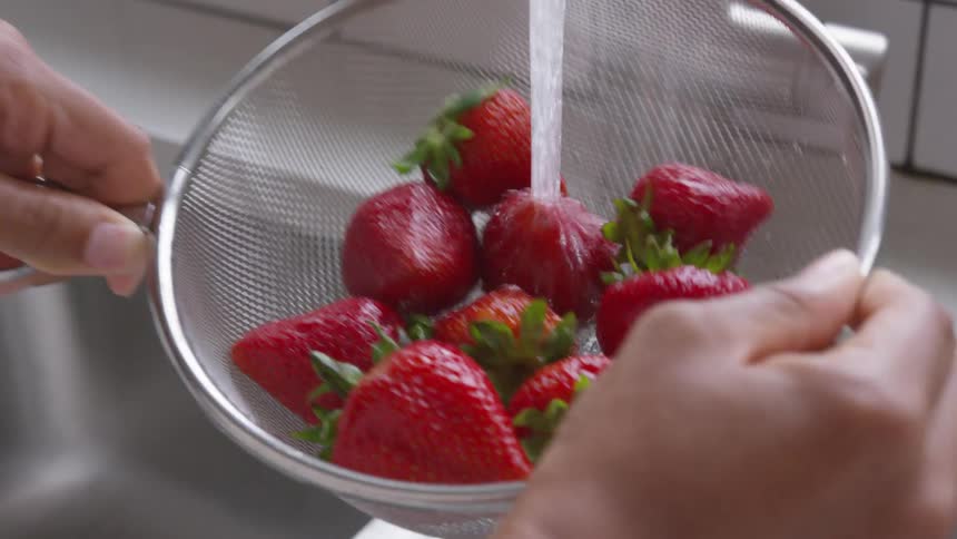 A person is washing strawberries in the sink