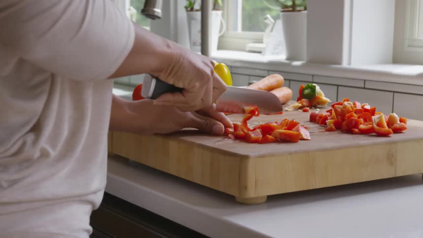 A woman cuts vegetables atop a large cutting board on her kitchen counter