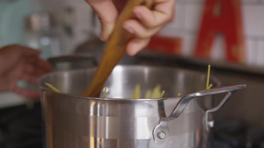 A woman stirs spaghetti in a large stainless steel pot in her kitchen
