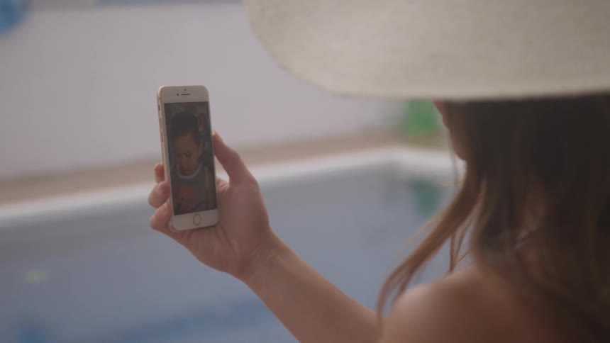 A woman looks at a toddler on her cell phone