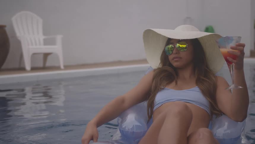 A young woman floats in a swimming pool while holding a cocktail