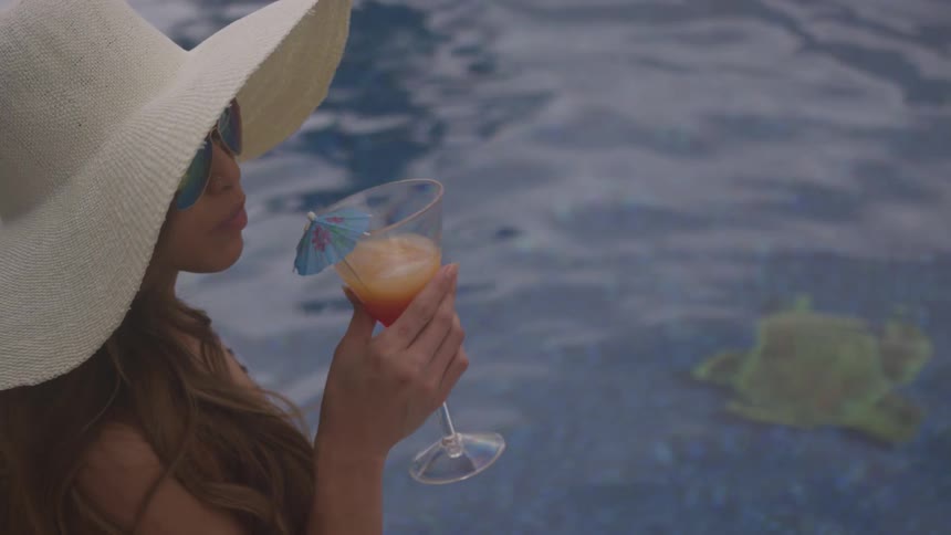 A young woman in a swimming pool sips on a cocktail