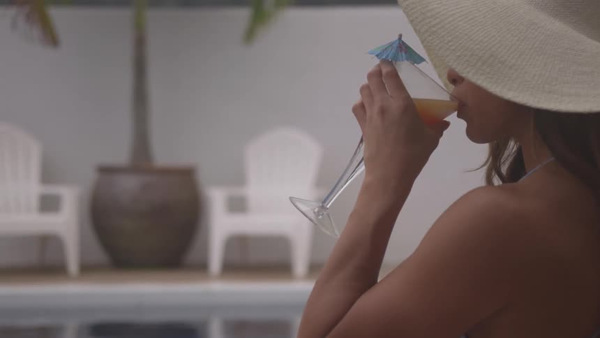 A young woman sits in a pool and sips on a cocktail