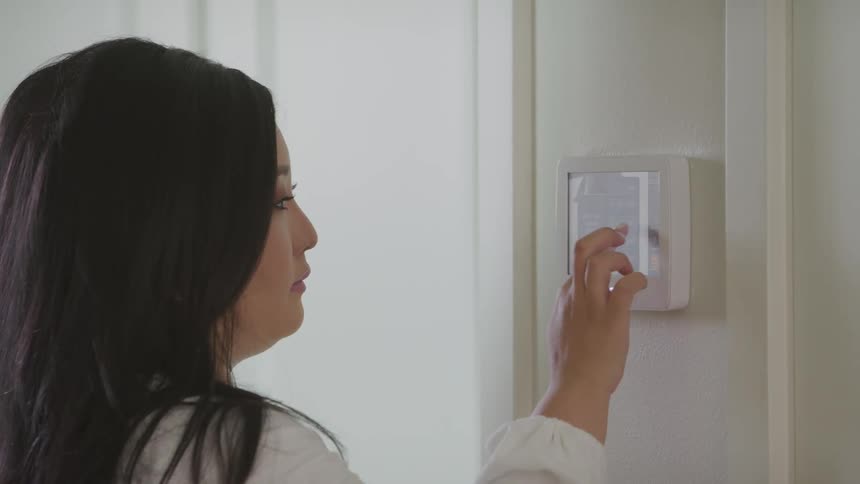 A woman uses her fingers to input some options on a touch screen smart home device