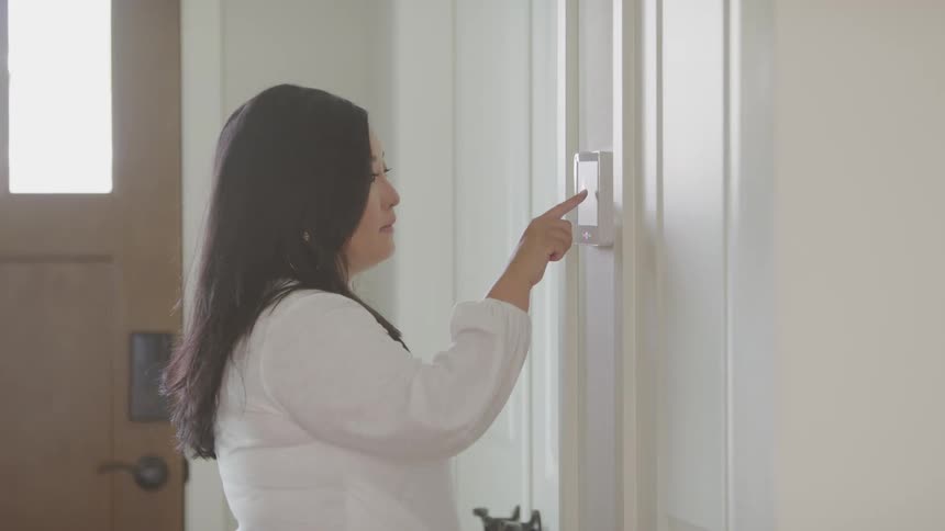 Female touches the security system pad hanging on the wall in the foyer before turning and walking towards the front door