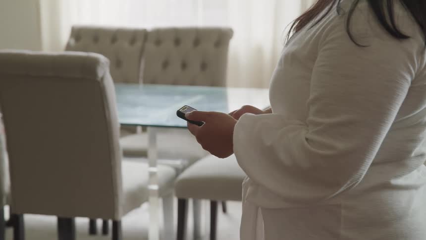A woman in a bathroom scrolls and taps on her smartphone before walking out of frame
