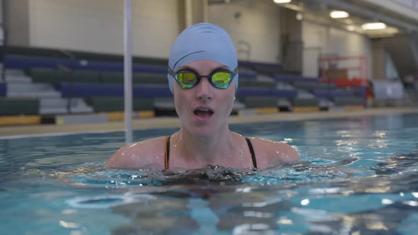 A woman in a large indoor pool puts on swimming goggles and descends into the water